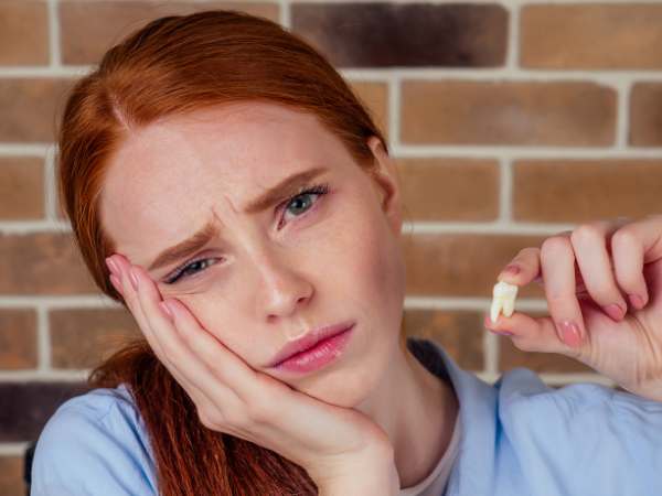 Distressed woman holding a tooth in one hand while touching the side of her face with the other hand